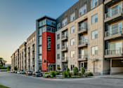 Thumbnail 1 of 36 - A street view of a row of apartment buildings with cars parked on the side.