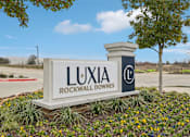 Thumbnail 34 of 34 - A sign for Luxia Rockwall Downes in front of a tree and a fence.