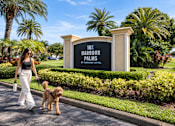 Thumbnail 2 of 52 - A woman walking her dog in front of a sign that says 10x Harbour Palms.