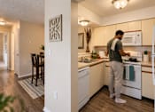 Thumbnail 6 of 52 - A man is standing in a kitchen with white appliances and wooden floors.