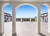 Thumbnail 15 of 40 - A courtyard with white arches and a clear blue sky.
