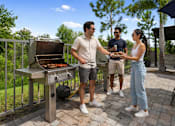 Thumbnail 19 of 59 - A man and woman are standing on a patio with a grill, the man is holding a pair of tongs.