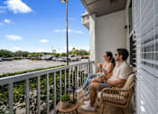 Thumbnail 36 of 59 - A man and woman are sitting on a balcony with a view of a parking lot.