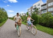 Thumbnail 3 of 59 - A man and woman ride bicycles down a path with a dog in a basket.