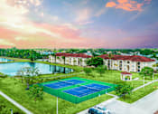 Thumbnail 2 of 33 - A tennis court is surrounded by a grassy area and a lake, with a building in the background.