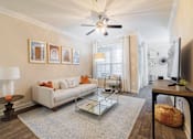 Thumbnail 15 of 30 - A living room with a white couch, a coffee table, and a ceiling fan.
