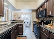 Thumbnail 16 of 30 - A kitchen with brown cabinets and black appliances.