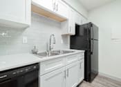 Thumbnail 4 of 17 - A kitchen with white cabinets and a black refrigerator.