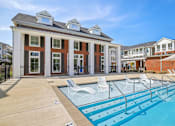 Thumbnail 25 of 39 - A pool area with a building and lounge chairs.