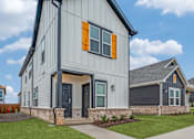 Thumbnail 19 of 20 - A modern house with a grey and white exterior and orange window shutters.