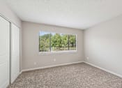 Thumbnail 6 of 16 - A room with a carpeted floor and a window showing a view of trees and a fence.