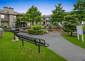 Thumbnail 16 of 28 - a park with a playground and benches and buildings in the background