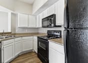 Thumbnail 4 of 24 - A black refrigerator is in a kitchen with white cabinets.