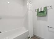 Thumbnail 24 of 38 - A white bathroom with a white tub and a green towel hanging on the towel rack.