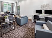 Thumbnail 6 of 25 - A living room with a grey couch, a glass coffee table, and a TV on a desk.