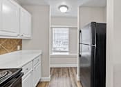 Thumbnail 38 of 54 - A kitchen with a black fridge, white cabinets and a stove top.