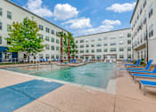 Thumbnail 6 of 19 - A large swimming pool surrounded by blue lounge chairs and palm trees.