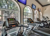 Thumbnail 12 of 25 - A gym with treadmills and a TV mounted on the wall.