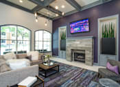 Thumbnail 8 of 25 - A living room with a grey couch, a coffee table, a fireplace, and a flat screen TV mounted on the wall.