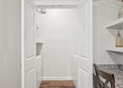 Thumbnail 17 of 34 - A white hallway with a wooden floor and a chair on the right side.