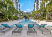 Thumbnail 18 of 25 - an outdoor pool with chairs and palm trees in an apartment building