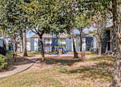 Thumbnail 38 of 38 - A playground with a slide is surrounded by trees and a building in the background.