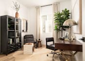 Thumbnail 7 of 19 - A black bookcase with a plant on top sits next to a desk with a lamp and chair.