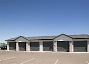 Thumbnail 10 of 21 - A building with a black roof and grey walls with a parking lot in front.