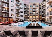 Thumbnail 15 of 26 - A swimming pool surrounded by lounge chairs in front of apartment buildings.