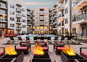 Thumbnail 17 of 26 - A fire pit in the middle of a courtyard surrounded by chairs and buildings.