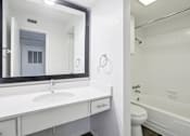 Thumbnail 5 of 21 - A white bathroom with a sink, mirror, toilet and bathtub.