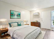 Thumbnail 13 of 17 - A bedroom with a large bed, a nightstand with a lamp, and a painting on the wall.