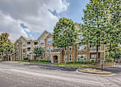 Thumbnail 3 of 37 - A large apartment complex with a parking lot in front.