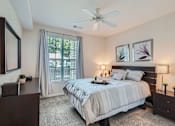 Thumbnail 18 of 37 - A bedroom with a large bed, a ceiling fan, and a window with curtains.