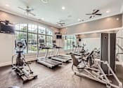 Thumbnail 32 of 37 - A spacious home gym with a television, exercise equipment, and a window.