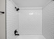 Thumbnail 45 of 54 - A white tiled shower stall with black handles.