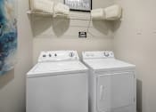 Thumbnail 16 of 25 - A white washing machine and dryer in a small laundry room.