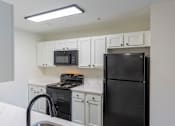 Thumbnail 16 of 40 - A black refrigerator sits in a kitchen with white cabinets and a black stove.