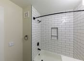 Thumbnail 14 of 40 - A white tiled shower with a white tub and a black shower head.
