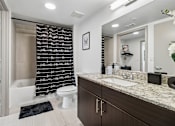 Thumbnail 13 of 34 - A bathroom with a white toilet, a sink, and a shower with a black and white curtain.