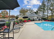 Thumbnail 21 of 45 - A pool area with chairs and umbrellas is surrounded by trees.