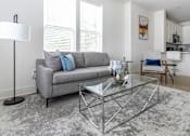 Thumbnail 10 of 11 - A modern living room with a grey sofa and a glass coffee table.