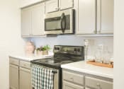Thumbnail 7 of 34 - a kitchen with white cabinets and a stove and microwave