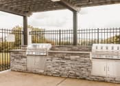 Thumbnail 31 of 34 - two outdoor barbecue grills next to a stone wall with a pavilion