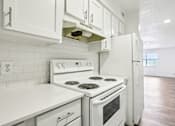 Thumbnail 6 of 21 - A white kitchen with a stove and refrigerator.