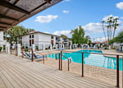Thumbnail 23 of 26 - A wooden deck with a pool and a building in the background.