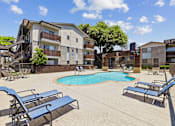 Thumbnail 32 of 38 - A pool surrounded by lounge chairs in front of apartment buildings.