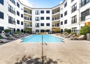 Thumbnail 22 of 37 - a swimming pool with chaise lounge chairs and an apartment building in the background