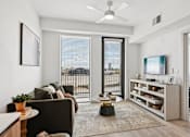 Thumbnail 9 of 26 - A living room with a brown couch, a coffee table, a television, and a balcony with a view of the city.