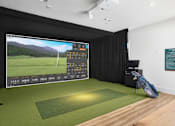Thumbnail 31 of 47 - A golf simulator room with a screen showing a golf course and a bag of clubs on the floor.